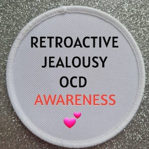 May include: White round patch with the text "Retroactive Jealousy OCD Awareness" in black and red lettering. Two pink hearts are at the bottom of the patch.
