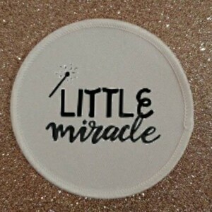 May include: White round fabric patch with black embroidery that reads "LITTLE miracle" with a small stick figure holding a star above the text.