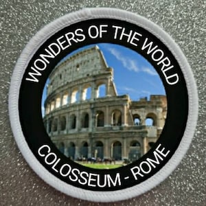 May include: A white round patch with black text and a photo of the Colosseum in Rome. The text reads "Wonders of the World Colosseum - Rome".