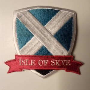 May include: A white and blue embroidered patch with a white X on a blue background. The patch has a red banner with the text "ISLE OF SKYE" in white.