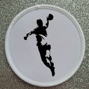 May include: White round patch with a black silhouette of a person throwing a ball. The person is in mid-air with their arm extended and the ball is in the air.