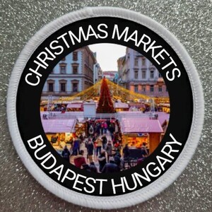 May include: A white and black circular patch with the text "Christmas Markets Budapest Hungary" around the edge. The center of the patch features a photo of a Christmas market in Budapest, Hungary.