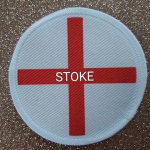 May include: A white round patch with a red cross in the center. The word "STOKE" is printed in black letters below the cross.