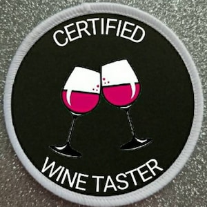 Puede incluir: Un parche redondo blanco con texto negro que dice "CERTIFIED WINE TASTER" y dos copas de vino rosadas con vino tinto dentro, chocando entre sí.