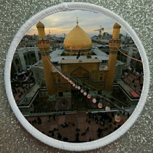 May include: An aerial view of a golden dome mosque with two minarets. The mosque is surrounded by a crowd of people and decorated with strings of lights.