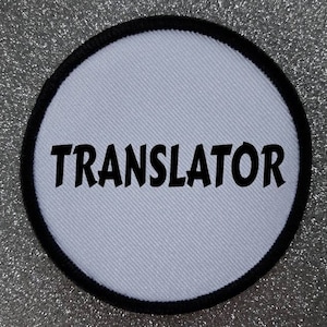 May include: White round iron-on patch with a black border and the word "TRANSLATOR" in black text.