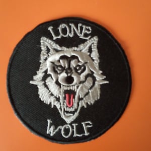 May include: A black and white embroidered patch featuring a wolf's head and the words "LONE WOLF" in white.