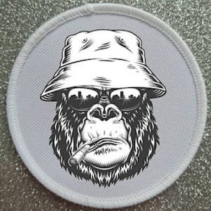 Puede incluir: Una ilustración en blanco y negro de un gorila con gafas de sol y un sombrero de pescador, fumando un cigarrillo. El gorila mira directamente al espectador.