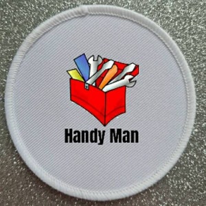 Peut inclure: Un écusson rond gris avec une bordure blanche cousue. L'écusson présente un dessin de boîte à outils rouge remplie d'outils et le texte "Handy Man" en noir.