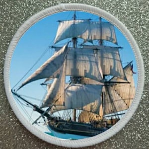 May include: A white sailing ship with multiple sails, set against a blue sky with white clouds. The ship is in the water, with the bow of the ship facing the viewer.