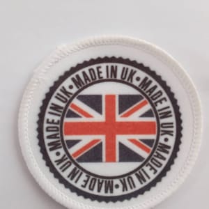 Op de afbeelding: Een ronde witte patch met een zwarte rand en de tekst "MADE IN UK-MADE IN UK-MADE IN UK-MADE IN UK-MADE IN UK" rond een rood, wit en blauwe Union Jack vlag.