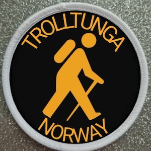 Könnte beinhalten: Ein weißer runder Patch mit schwarzem Hintergrund. Der Patch zeigt eine gelbe Strichmännchenfigur beim Wandern mit Rucksack und Wanderstock. Der Text "Trolltunga Norway" ist in Gelb um die Figur herum geschrieben.