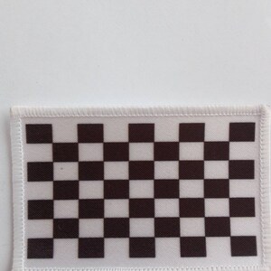 May include: A rectangular patch with a black and white chequered pattern. The patch has a white border with a stitched edge. The chequered design is made up of alternating black and white squares.