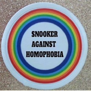 Puede incluir: Un parche circular blanco con un borde de arcoíris. El centro del parche tiene el texto "Snooker Against Homophobia" en negro.