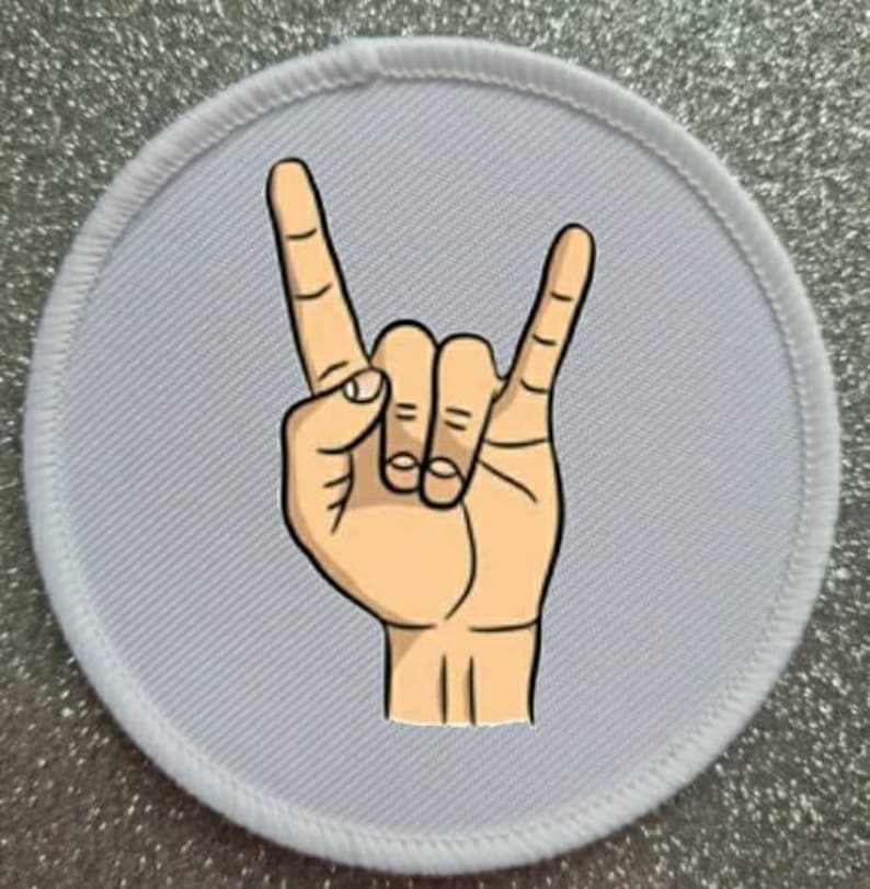 Pode incluir: Etiqueta redonda branca para passar a ferro com uma m&atilde;o de desenho animado fazendo o gesto de rock and roll.