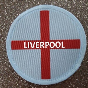 May include: A white circular patch with a red cross and the word "LIVERPOOL" in the center.