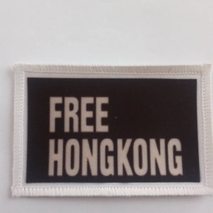 Puede incluir: Parche de tela blanco con fondo negro y texto blanco que dice "FREE HONGKONG".