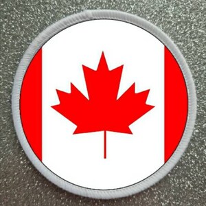 May include: A white circle patch with a red maple leaf in the center and a red stripe on each side. The patch has a white border.