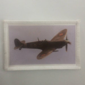 May include: A brown and white aeroplane with red markings on the wings and tail. The aeroplane is flying in the sky.