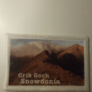 Può includere: Toppa ricamata bianca con una foto di una catena montuosa e il testo "Crib Goch Snowdonia" in bianco.