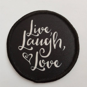May include: A round, black patch with the words "Live, Laugh, Love" in white script. A small white heart is included in the design. The patch has a black stitched border.