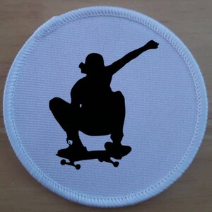 Könnte beinhalten: Runder Stoff-Patch in Weiß mit einer schwarzen Silhouette einer Person beim Skateboarden.