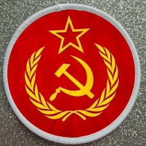 Puede incluir: Un parche circular rojo con un martillo y una hoz amarillos, una corona de laurel amarilla y una estrella roja en el centro.