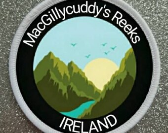 Peut inclure: Écusson rond blanc avec une bordure noire et le texte "MacGillycuddy's Reeks Ireland". L'écusson représente une chaîne de montagnes vertes avec une rivière bleue et un soleil jaune dans un ciel bleu.