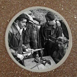 May include: A group of men in military uniforms stand together holding a rifle. The men are wearing hats and jackets. The rifle is a black and silver submachine gun.