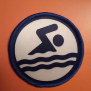 May include: Blue and white round patch with a swimmer icon and wavy lines. The swimmer is in a diving pose with a head and body silhouette.