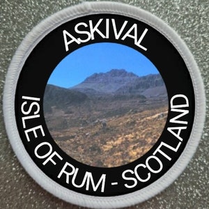 Op de afbeelding: Een ronde witte patch met zwarte tekst en een foto van een bergketen. De tekst luidt "Askivall Isle of Rum - Scotland".