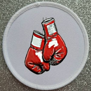 Könnte beinhalten: Ein runder weißer Aufnäher mit einem roten und weißen Boxhandschuh-Design. Die Handschuhe hängen oben am Aufnäher.
