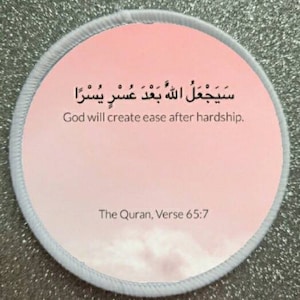 Puede incluir: Una pegatina redonda con borde blanco y fondo degradado rosa y blanco. La pegatina presenta una frase árabe en texto negro, "سَيَجْعَلُ اللَّهُ بَعْدَ عُسْرِ يُسْرًا", que se traduce como "Dios creará la facilidad después de la dificultad." La pegatina también incluye el texto "El Corán, Versículo 65:7" en texto negro.
