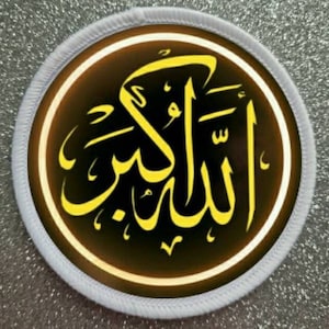 May include: A white circular patch with a black and yellow design. The design is the Arabic word "Allah" in a stylized font.