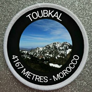 Könnte beinhalten: Runder weißer und schwarzer Patch mit einem Foto einer schneebedeckten Bergkette. Der Text lautet "TOUBKAL 4167 METER - MAROKKO".