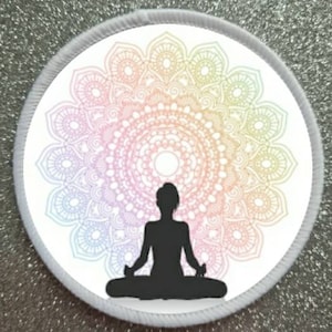 May include: A white round patch with a colorful mandala design and a black silhouette of a person sitting in a yoga pose in the center.