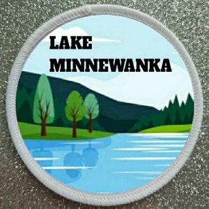 May include: A white round patch with a blue and green landscape design. The text "LAKE MINNEWANKA" is printed in black at the top of the patch.