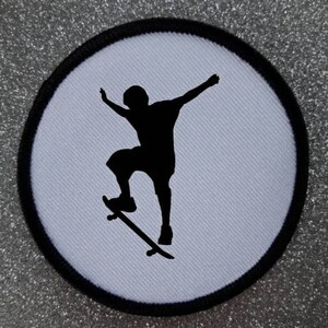 May include: A black and white silhouette of a person skateboarding on a white background. The image is on a round, black-bordered patch.