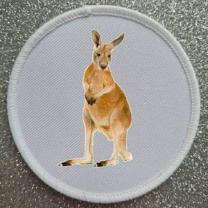 Può includere: Un cerotto di stoffa bianco con un canguro marrone in piedi su uno sfondo bianco.