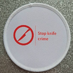 May include: White round fabric patch with a red circle and a diagonal line through it, symbolizing a no knife sign. The text "Stop knife crime" is printed in red letters below the symbol.
