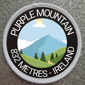 May include: A white and black round patch with the text "Purple Mountain 832 Metres - Ireland" and a cartoon illustration of a mountain with a blue sky and white clouds.