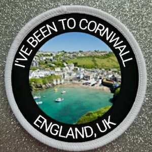 May include: Circular patch with a black border and white stitching. The patch features a scenic image of a coastal town with boats on the water. Text around the image reads "I'VE BEEN TO CORNWALL ENGLAND, UK."