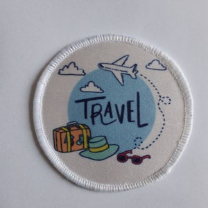 Può includere: Cerotto rotondo bianco con un cerchio blu e la parola "TRAVEL" in bianco. Il cerchio contiene un aereo, nuvole, una valigia, un cappello e occhiali da sole.