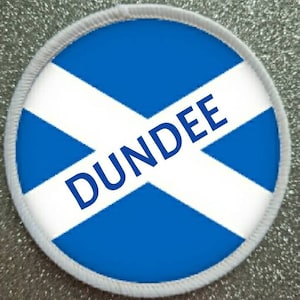 May include: A white and blue round patch with a white cross on a blue background. The word "DUNDEE" is written in blue letters across the cross.