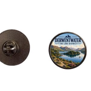 Könnte beinhalten: Ein runder Metall-Ansteckpin mit einer Landschaftsillustration von Derwentwater im Lake District. Das Bild zeigt einen blauen See, Berge und ein kleines Segelboot. Der Text lautet Derwentwater The Lake District. Die Rückseite hat einen Verschluss.