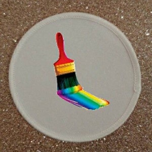 May include: A white round patch featuring a rainbow paintbrush design. The paintbrush is red, black, yellow, green, blue, indigo, and violet.