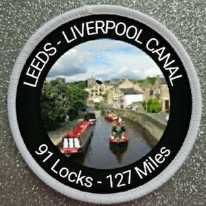 May include: A white and black round patch with the text "Leeds-Liverpool Canal 91 Locks - 127 Miles" and a photo of a canal with boats.