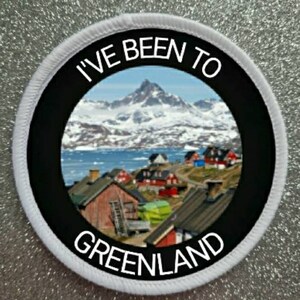 Puede incluir: Parche redondo blanco con borde negro y el texto "I've Been To Greenland". El centro presenta una foto de una cordillera nevada y un pequeño pueblo.