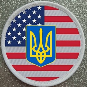 May include: A white circular patch with a red, white and blue American flag on the left side and the Ukrainian coat of arms, a yellow trident on a blue shield, on the right side.
