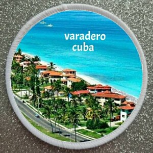 May include: A white round patch with a blue and white image of a beach scene with palm trees and buildings. The text "varadero cuba" is printed in white on the patch.